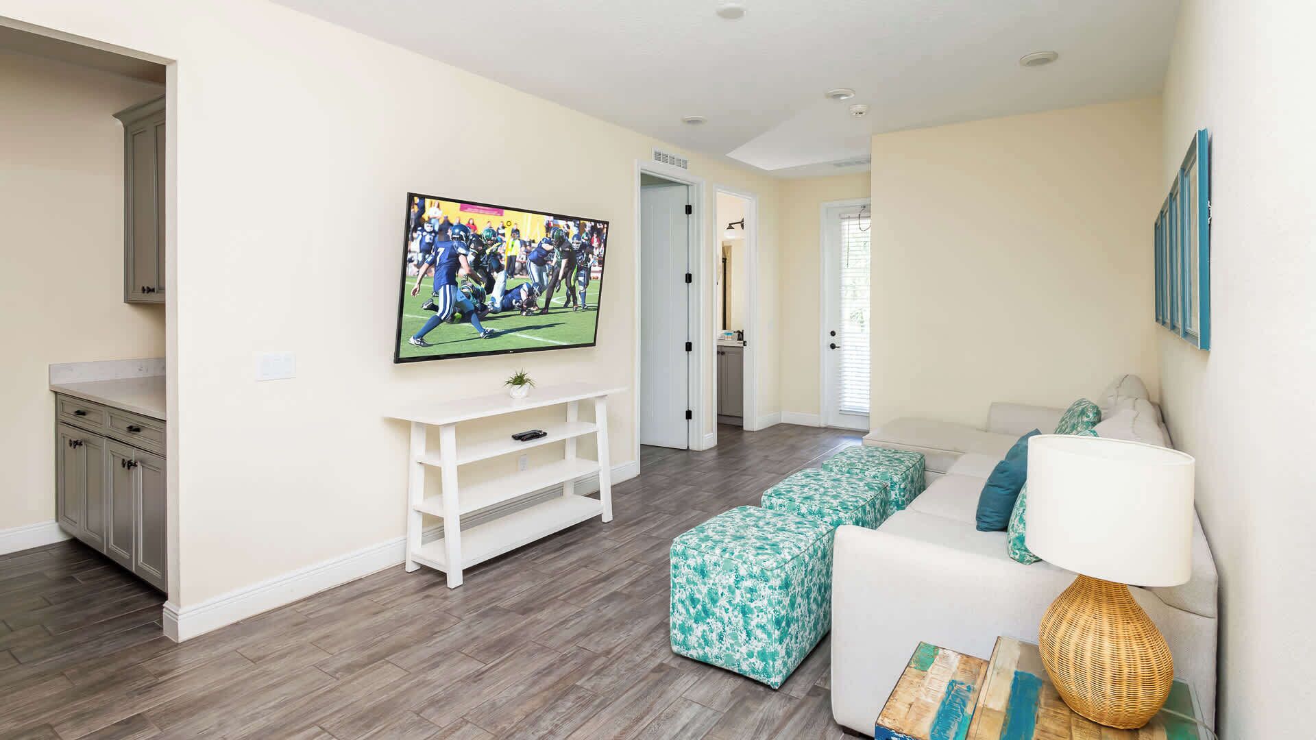 Una sala de estar con televisor, sofá, mesa de centro y una puerta que da a otra habitación.