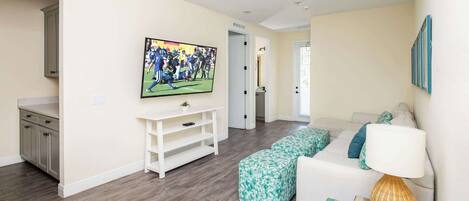 Una sala de estar con televisor, sofá, mesa de centro y una puerta que da a otra habitación.
