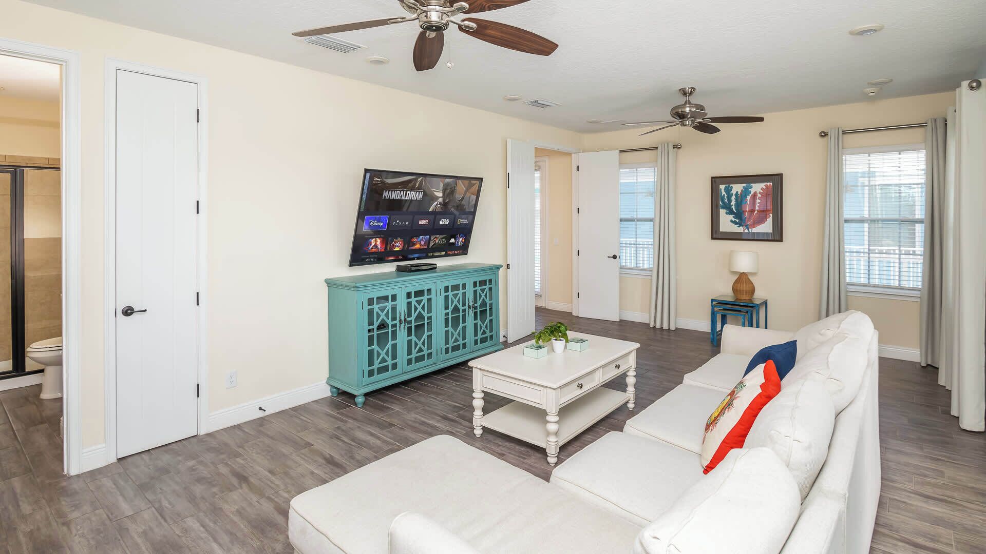 A living room with a white sofa, teal cabinet, and a television displaying 'Mandalorian'.