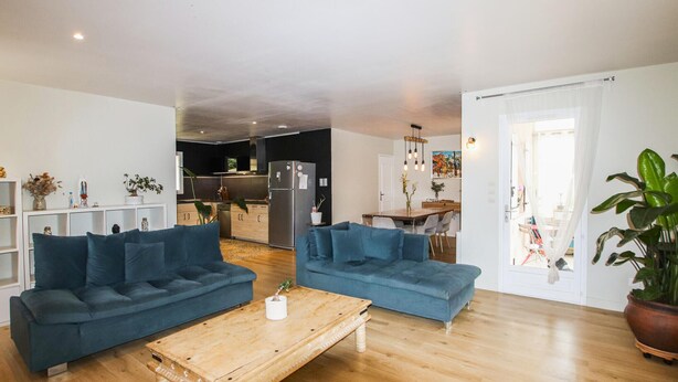 Een moderne woonkamer met twee blauwe banken, een houten salontafel en een keuken op de achtergrond.
