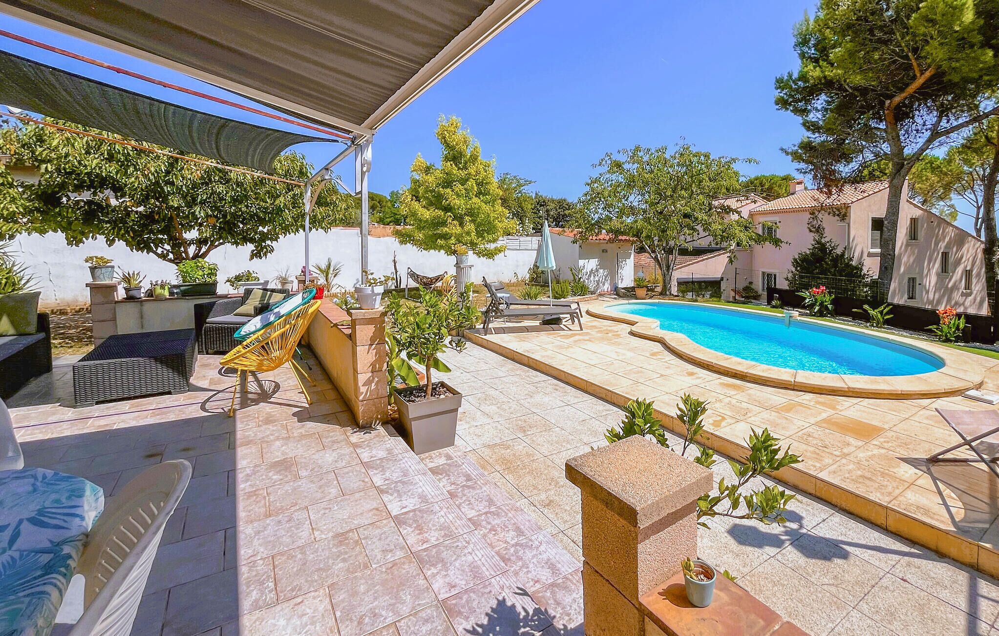 A pool area with a tiled deck, lounge chairs, and potted plants.
