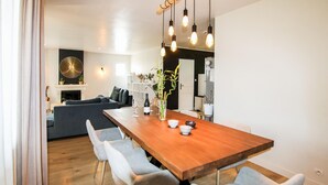 Een moderne eetruimte met een houten tafel, lichtgrijze stoelen en hangende pendelverlichting.
