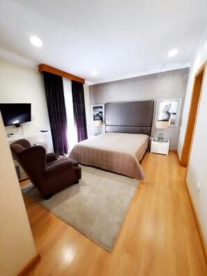 Una moderna camera d'hotel con un letto grande, una scrivania, una sedia, una televisione e un piccolo tavolino con una lampada.