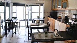 A modern kitchen with wooden cabinets, a black countertop, and a built-in oven. There is a dining area with a table and chairs, and a large window providing natural light. - Milfontes Guest House (Odemira)