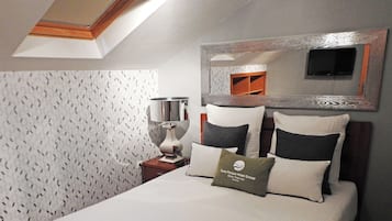 A hotel room with a bed, pillows, a nightstand, a lamp, and a mirror.