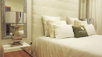 A hotel room with a bed, pillows, a bedside table, a mirror, and a lamp.