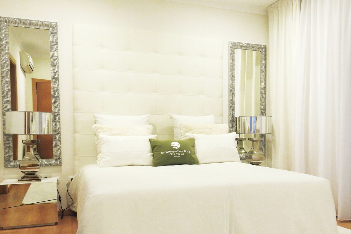 A hotel room with a large bed, two bedside lamps, a mirror, and a pillow with the hotel's logo.