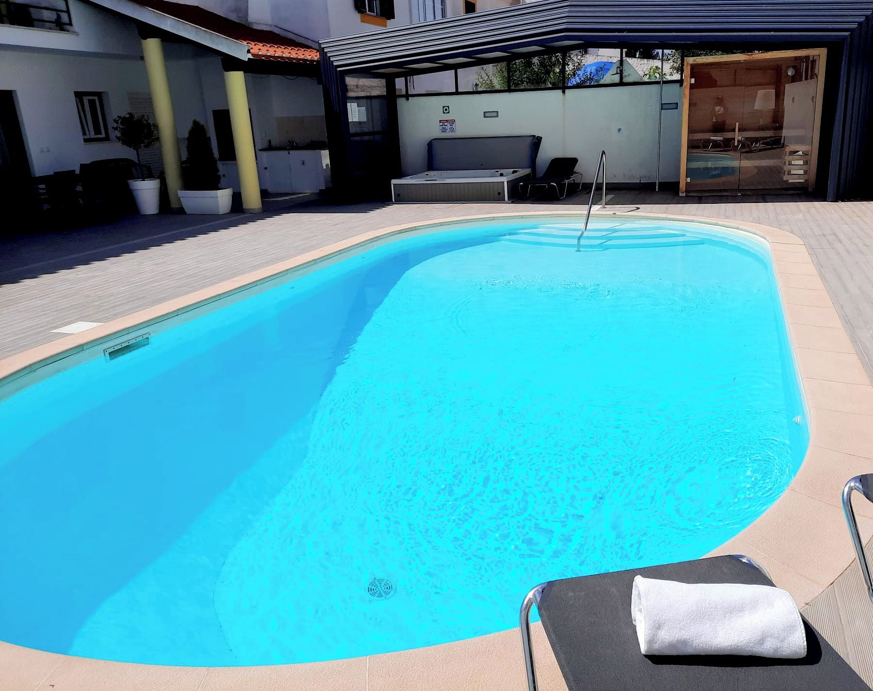 A swimming pool with a lounge chair and a towel, surrounded by a covered patio area.