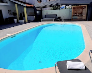 Una piscina con una silla de descanso y una toalla, rodeada por un porche cubierto.