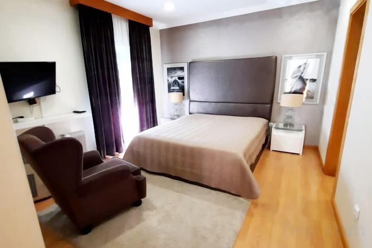 A hotel room with a large bed, a flat-screen TV, a desk, and a chair.