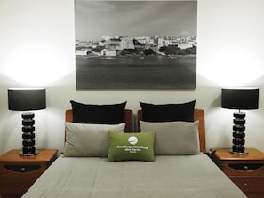 Un dormitorio con una cama, dos mesitas de noche, dos lámparas y un cuadro de paisaje urbano en la pared.