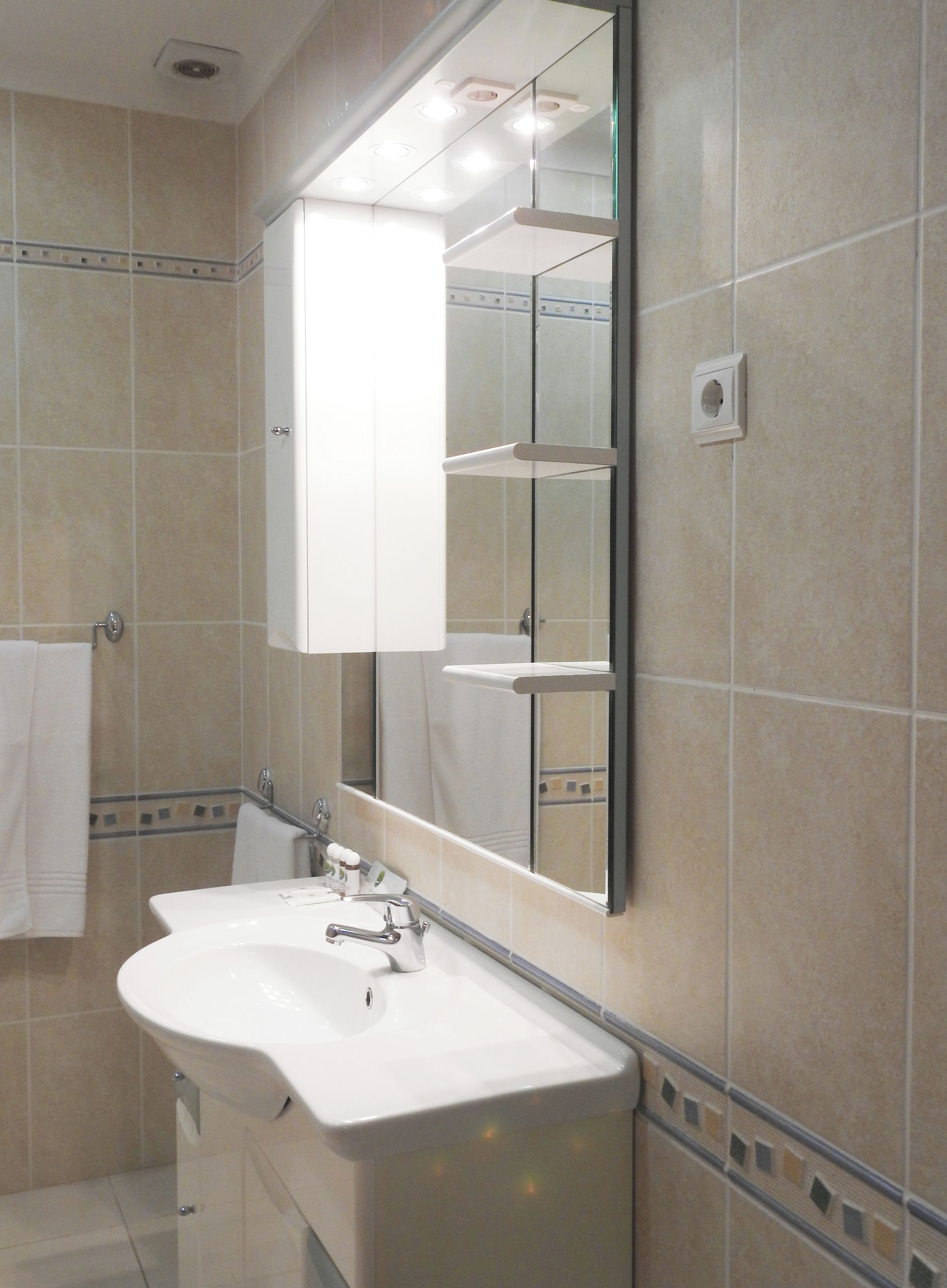 A bathroom with a white sink, mirror, and tiled walls.