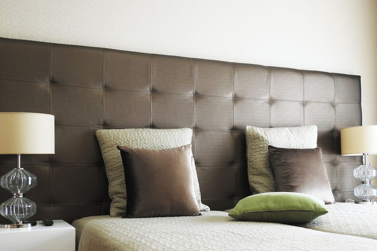 Een hotelkamer met een gestoffeerd hoofdeinde, twee bedlampen en een bed met een gewatteerde deken.