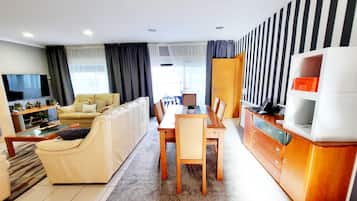 A modern living room with a sofa, TV, dining table, and kitchen area.