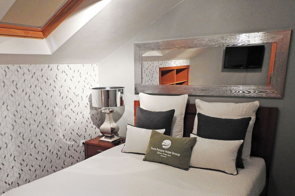 Quarto de hotel com cama, almofadas, mesa de cabeceira, abajur e espelho.