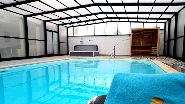 An indoor swimming pool with a glass ceiling, a wooden bench, and a towel with a logo. - Milfontes Guest House (Odemira)