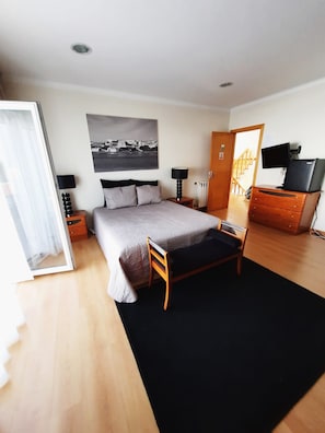 A bedroom with a bed, bedside tables, a dresser, a TV, and a cityscape painting.