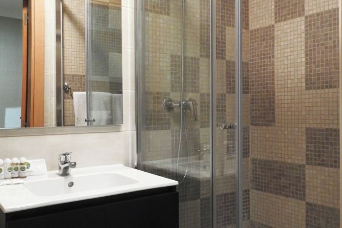 A bathroom with a glass shower enclosure, a white sink, and a tiled wall.