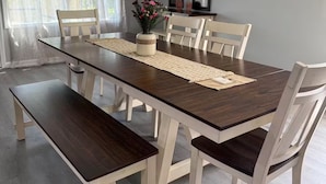 Een eethoek met een rechthoekige tafel, witte stoelen, een bank en een vaas met bloemen.