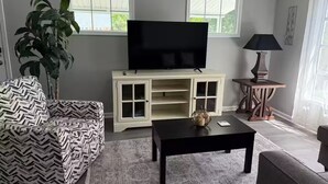 Een woonkamer met een bank, een salontafel, een televisie op een kast, een lamp en een plant.