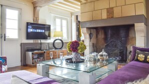 Una sala de estar con una mesa de centro de vidrio, un sofá, una chimenea, un televisor y una estantería.