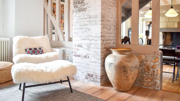 Una habitación acogedora con un sillón mullido, un jarrón grande y una pared de ladrillo rústico.