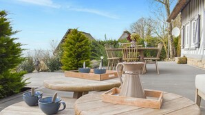 Un patio con mesas y sillas de madera redondas, una mesa auxiliar de madera y una jarra de cerámica.