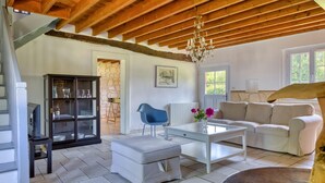 A spacious living room with a high wooden ceiling, a glass coffee table, a white sofa, and a blue chair.