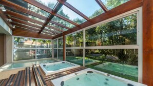 Et spa-område med to boblebade under et glastag, omgivet af en træterrasse og udsigt til en have.