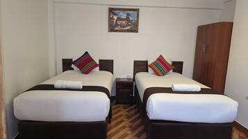 A hotel room with two beds, a wooden wardrobe, a nightstand, and a painting on the wall.