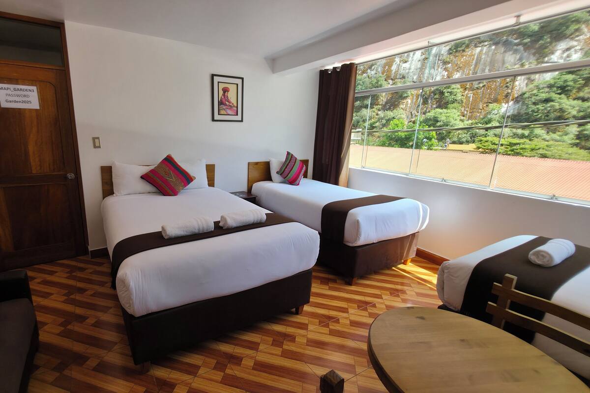 A hotel room with two beds, a wooden floor, a large window with a view, and a door with a sign.