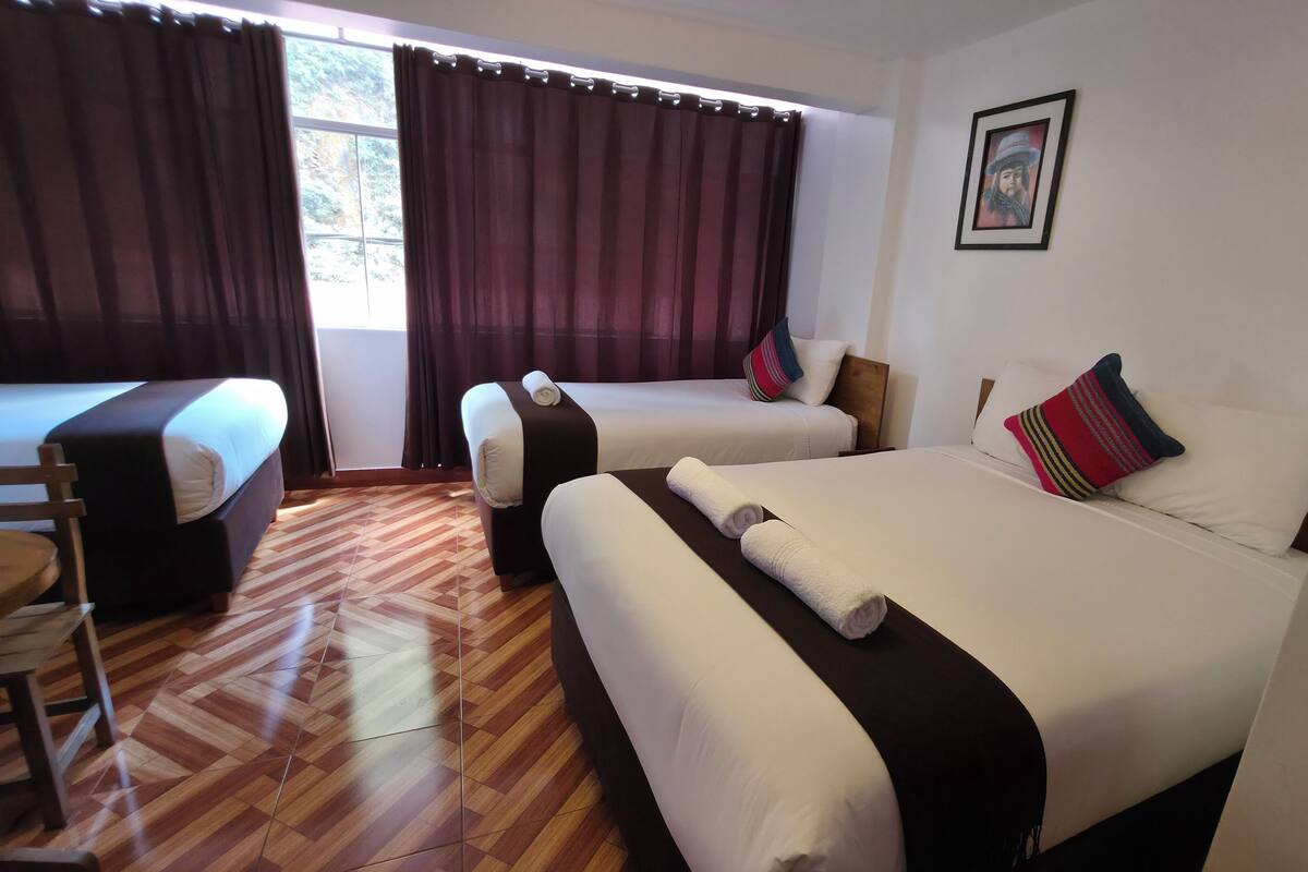 A hotel room with two beds, a wooden floor, and a window with curtains.