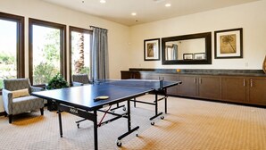 Une pièce avec une table de ping-pong, une chaise, un meuble et un grand miroir au mur.
