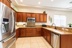Una cocina moderna con electrodomésticos de acero inoxidable, gabinetes de madera y encimeras de granito, además de un ventanal con persianas.