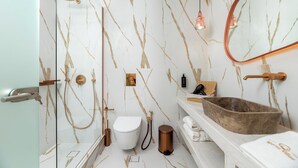Un baño con pared de mármol, inodoro blanco, lavabo de madera y un espejo.