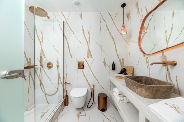 A bathroom with a marble wall, a white toilet, a wooden basin, and a mirror.