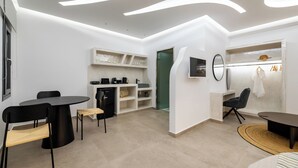 Una sala de estar moderna con una mesa de comedor redonda, sillas negras, una zona de cocina con armarios blancos y una puerta verde.