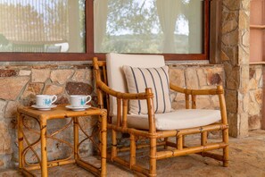 A wicker chair with a cushion and a small table with two cups, set against a stone wall with a window above. - BLUE BAY HOME just few steps from the bay of Porto Luna (Villasimius)