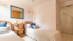 Quarto com duas camas de solteiro, mesa de cabeceira com luminárias, espelho e guarda-roupa.