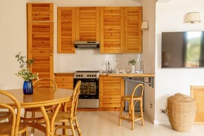 Une cuisine moderne avec des meubles en bois, un four encastré et un coin repas doté de chaises en osier.