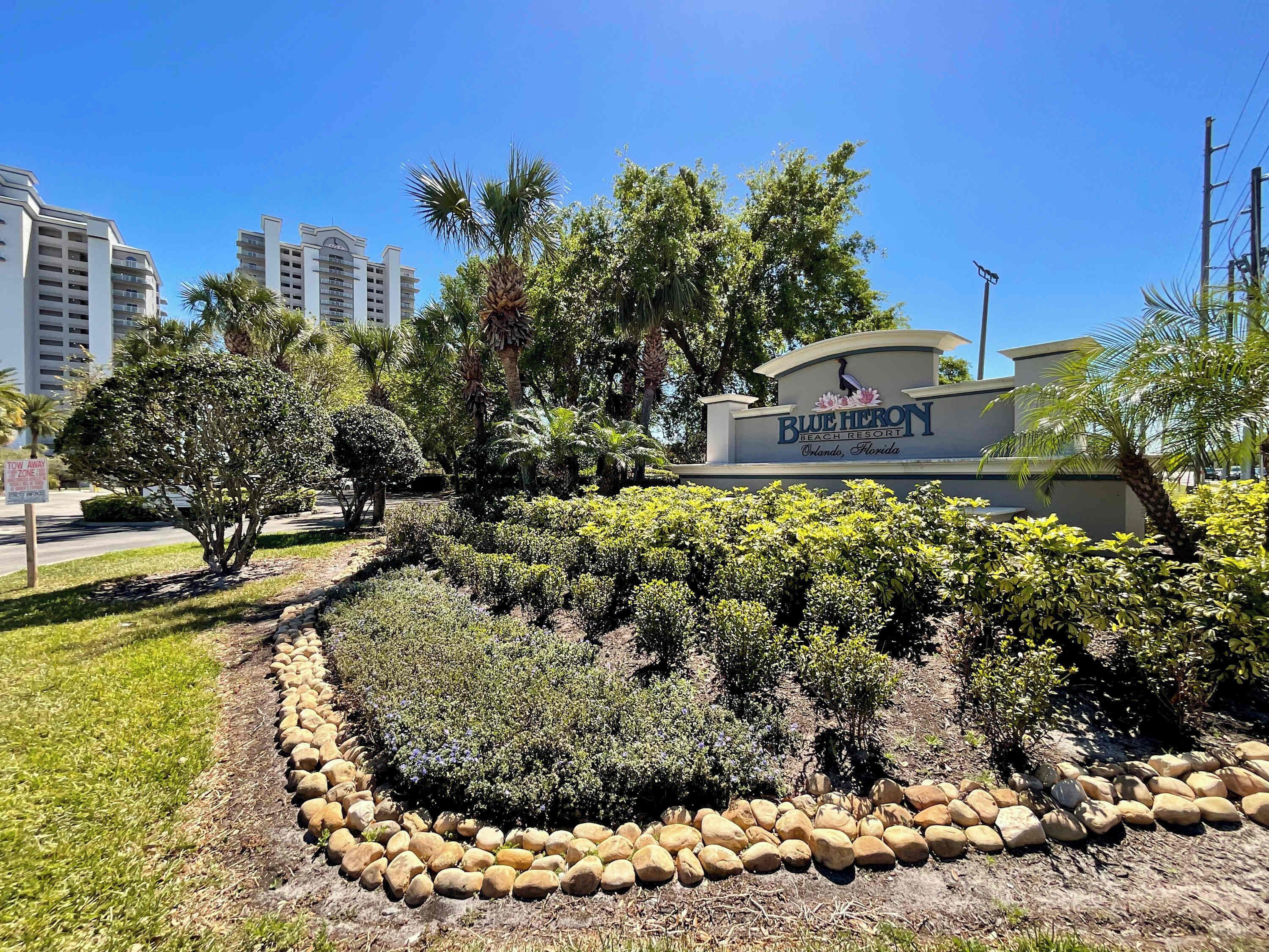 Un panneau indiquant l’emplacement du Blue Heron Beach Resort à Orlando, en Floride, entouré d’un aménagement paysager verdoyant et bordé de rochers.