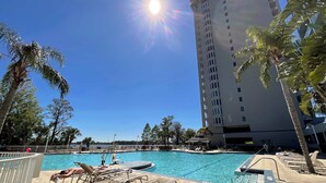 A hotel pool area with sunbathing chairs, a pool, and a tall building in the background. - Lake Views At Blue Heron (Orlando)