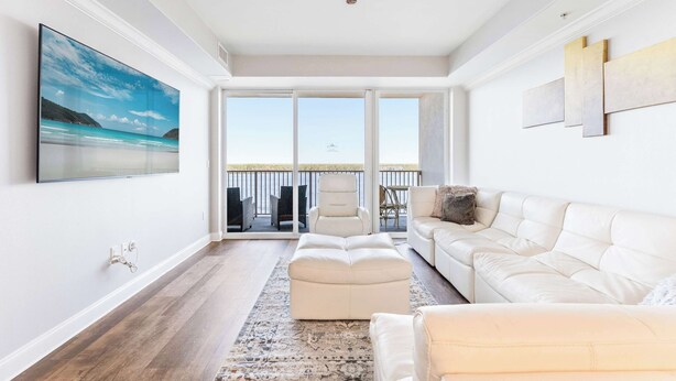 A spacious living room with a white sofa, a large armchair, and a coffee table. There is a large window with a view of the outdoors. - Lake Views At Blue Heron (Orlando)
