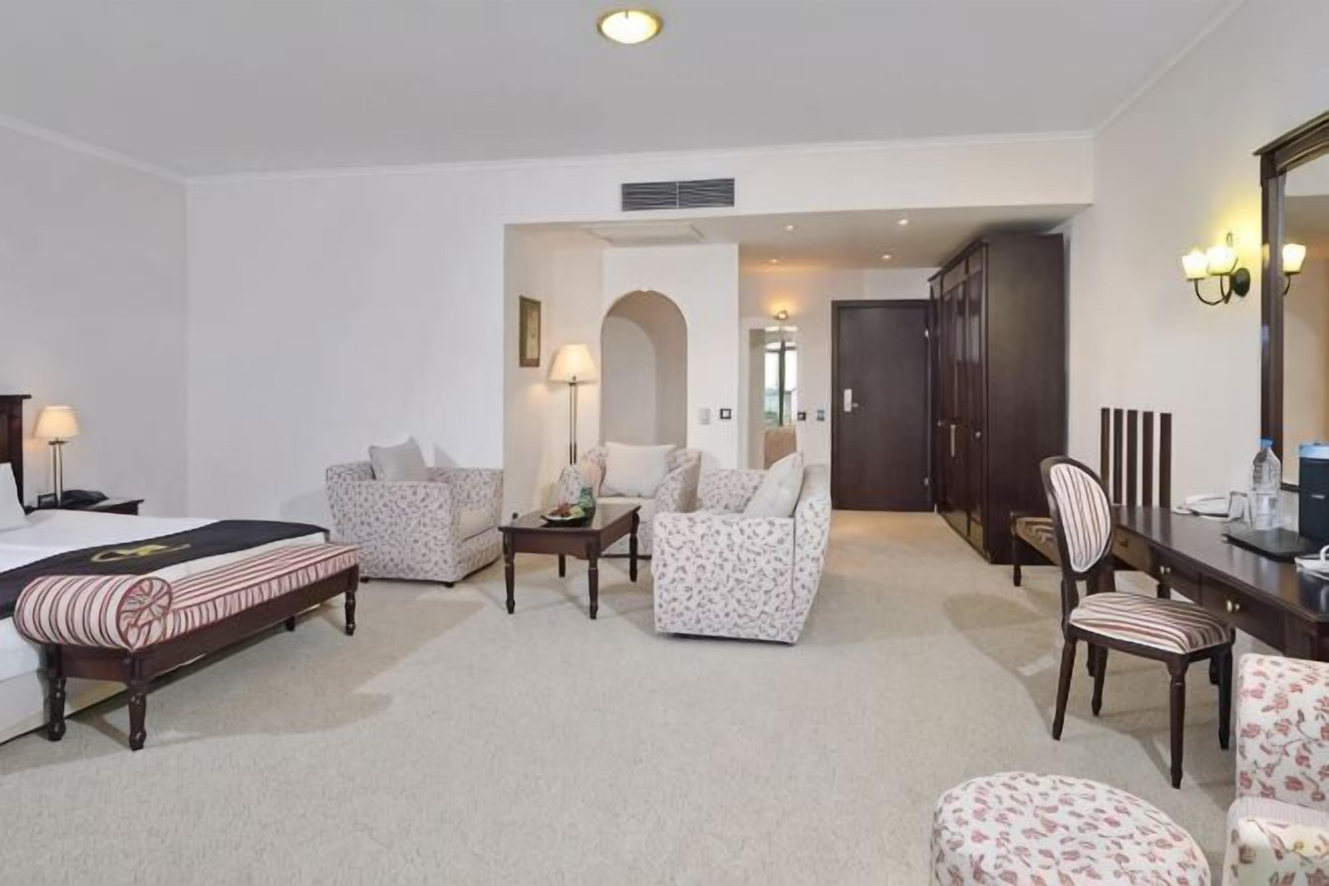 Une chambre d’hôtel comprenant un lit, deux fauteuils, un canapé, une table à manger et un miroir.