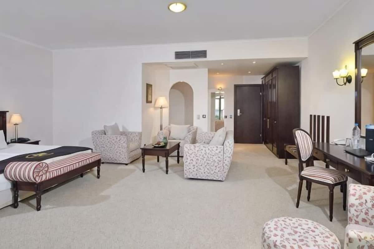 A hotel room with a bed, two armchairs, a sofa, a dining table, and a mirror.