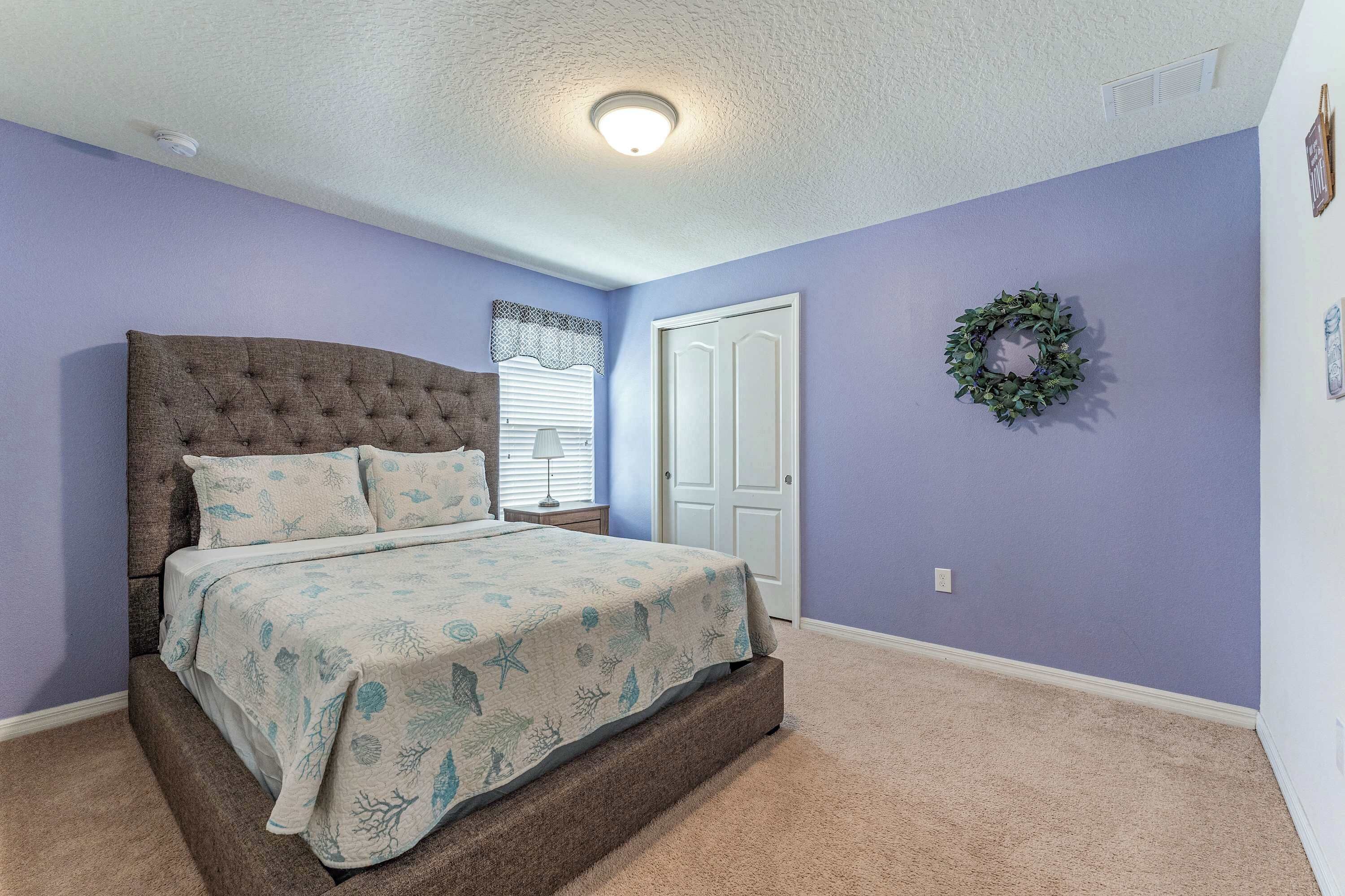 Un dormitorio con cabecera capitonada, cama con colcha floral, una puerta y un adorno colgante en la pared.