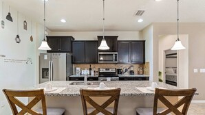 Una cocina con armarios oscuros, encimera de granito y tres sillas de madera con asientos acolchados.