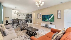 Un salón espacioso con sofá, mesa de centro y televisor. Hay un comedor con sillas y una mesa, y una cocina al fondo.