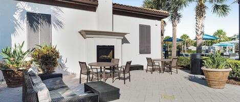 An outdoor patio with wicker furniture, a fireplace, and potted plants.