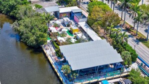 Un bâtiment situé au bord de la rivière, doté d’un espace extérieur couvert, d’un quai avec des bateaux et d’une route adjacente à l’eau.